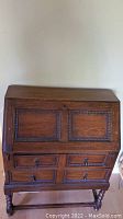 Front view of vintage wooden writer's desk showing the drop-down writing surface panel with carved decorative border, four drawers with knobs, and keyhole for lock.