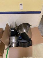 Various cookware pieces including pans and pots seen from above inside box.