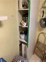 Tall white storage rack or shelving unit with kitchen appliances including a handheld mixer on the middle shelf and other kitchen tools.