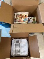 Box containing several assorted cookbooks with visible colorful covers including a couple on the top showing recipes and people.