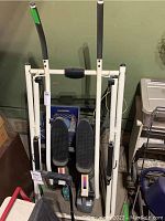 White glider elliptical exercise machine against a garage wall surrounded by other items.