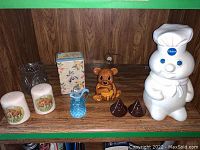 Display of all items on wooden shelf including two salt and pepper sets, cookie jars, candle holder, tin box, and Fenton glass jar.