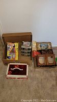 Overall view of box with PeeWee's Playhouse View-Master game, VHS tapes, trinket boxes, craft basket, and frames on carpeted floor