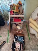 Overview photo showing gift wrapping supplies including gift bows, rolls of wrapping paper in tubes, a sponge toy dog with a colorful hat, a cardboard organizer, and other miscellaneous items on the floor near furniture.