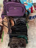 Photo showing the purple luggage pieces along with various black and brown bags stacked together on floor, highlighting zipper details and overall shape.