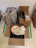Top-down view showing the fabric-lined woven basket with dish-drying mat, induction cooktop, cardboard boxes, and reusable shopping bag.