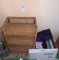 Rattan shelf with broken rattan pieces, scratches, and cookbooks in a box beside it.