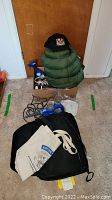 Green hooded sleeping bag partially inside a box along with cables and a blue portable Onn CD player, placed on carpet floor