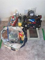 Photo showing contents of tool bag, fabric bag with additional items, and stapler with adhesives arranged on floor.