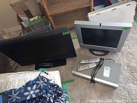 View of Samsung and Sanyo TVs with Philips combo player and remotes on floor.