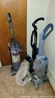 Three upright vacuum and carpet shampooers shown together upright and plastic bag containing vintage vacuum parts on carpet floor