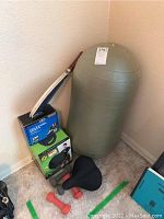 View showing inflatable exercise roller, racquet, boxes with weights and medicine ball, dumbbells, and bicycle seat on floor corner.