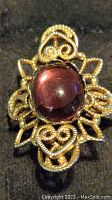 Front view showing a large red cabochon stone surrounded by ornate gold tone filigree work.