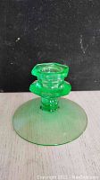 Side view of the green depression glass candleholder showing the wide circular base and hexagonal top for candle placement.
