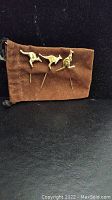 Photo of three gold-toned metal kangaroo hat pins arranged on brown pouch against black background