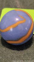 Close-up photo showing the blue marble with distinct orange swirls on the surface.