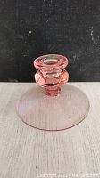 Pink depression glass candleholder with broad flat circular base and cylindrical top holder photographed from the side against a black background.