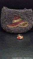 Photo of the vintage beaded purse with a hat embroidery design and the matching ring in front on a black background.