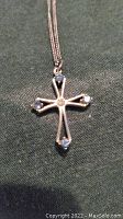 Photo of the full silver cross pendant on chain laid flat on dark fabric background
