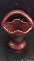 Front view of small vintage ceramic basket-shaped vase with handle and scalloped edge in reddish brown glaze.