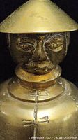 Close-up of the top half of a brass bell depicting an Asian figure wearing a conical hat, showing detailed facial features.
