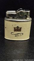 Full view of vintage lighter showing metal top and cream body with gold castle emblem