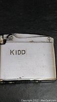 Front view of vintage silver-tone lighter with engraving 'KIDD'