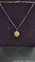 Full necklace with gold tone chain and hanging oval locket against black background