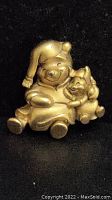 Close-up photo of gold-tone pin depicting Winnie The Pooh in a winter hat hugging Piglet.