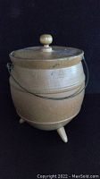 Side view of wooden butter churn with wire handle and lid with knob