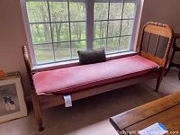 Full view of the vintage solid wood bench placed near window with pink cushion and small green pillow.