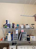 Wide view of wire shelves holding various cleaning and office supplies including detergents, drawer organizers, and small bottles.