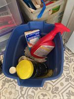 Blue mop bucket with cleaning liquids, red spray bottle and yellow container inside.