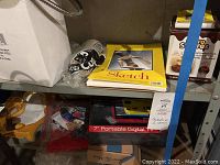 Shelf with the sketch pad, smores kit box, paint tubes, brushes, and plastic bag of small items.