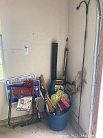 View of the lot showing the Easy-Go cart, garden shovel, shepherd's hook plant stand, folding chair, yard decor, umbrella, all placed in or near a blue bucket in the garage.