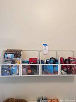 Wall-mounted white wire baskets holding a collection of miscellaneous household items including flashlights, dog treats, gift bags, and hardware items.