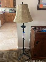 Full view of the black metal floor lamp with gold colored fabric lampshade, shown standing next to kitchen area.