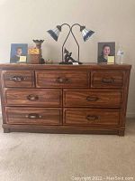 Front view of the wooden dresser showing seven drawers, darker wood top, and decorative objects on top.
