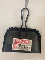 Large black metal dustpan with Farm & Ranch Agricultural Grade label and curved handle, hanging on wall