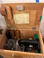 Opened wooden storage case showing Nikon microscope packed with protective padding and wooden accessory holders.
