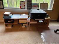 Two wooden desk top office shelves placed side by side near window; one has printer on top, the other has office papers.