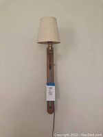 Front view of wooden wall sconce mounted on wall showing beige fabric shade and cord hanging below.