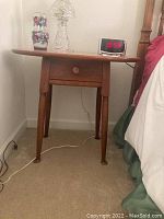 Front view of oval wooden accent table with drawer, decorative glass items, and digital clock on top.