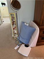 Photo showing the standing magnifying mirror, large wedge pillow, blue memory foam pillow, and white digital scale on the floor next to a wooden cabinet.