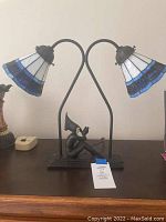 Front view of double Tiffany-style lamp showing blue and white stained glass shades and musician figurine base.