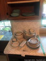 Full arrangement of all dishes in the lot showing multiple stacks of plates, bowls, cups and serving pieces on a kitchen counter.