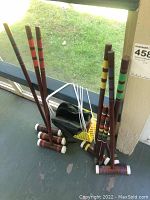 Photo showing the 6 wooden croquet mallets with colored bands and white capped ends alongside black carrying bag and wickets.