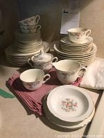 Stacked Eastern China porcelain cups, plates, saucers, sugar bowl with lid, and creamer with floral pattern and gold trim on a kitchen counter with cloth napkins.