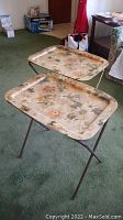 Photo showing side-by-side pair of folding snack trays with metal legs and floral motif