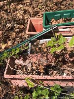 Group of assorted rectangular and square planting pots in red, brown, green, and pink colors with dried leaves inside, placed outdoors on ground with leaves around.